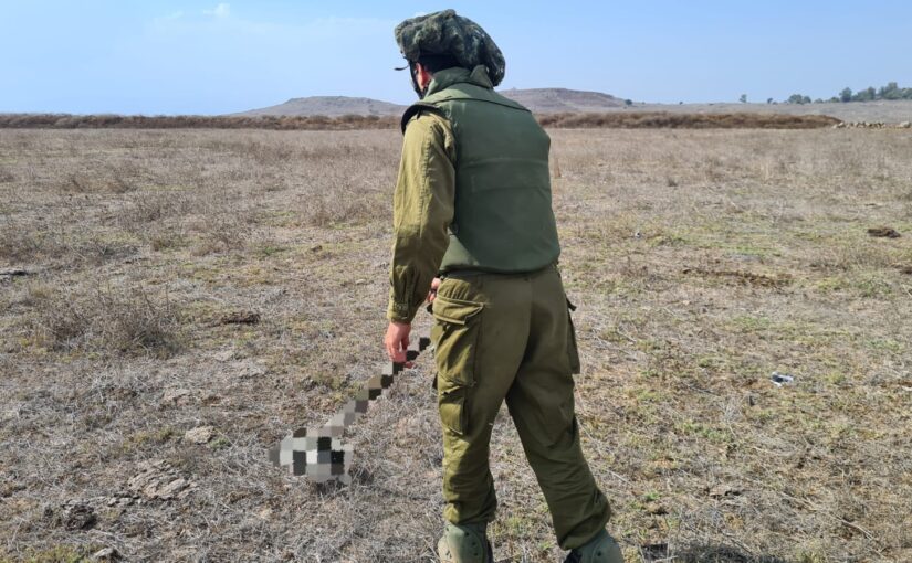 Using the metal detector on the field with a flak jacket, helmet, and safety glasses