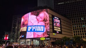 The advertisement screen on Azrieli center. On the left it says Getting them back and going back. On the right are the pics of the six hostages murdered by Hamas a week ago and the slogan Put an end to it, we are all the hostages families- back to Kaplan again 