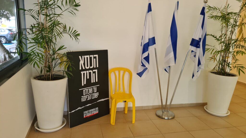 The empty chair with the sign next to it and some Israel flags on the other side